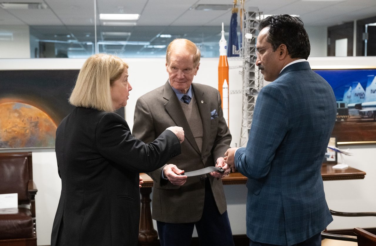 NASA and ISRO leaders discuss collaboration, seated at a conference table with flags in the background.