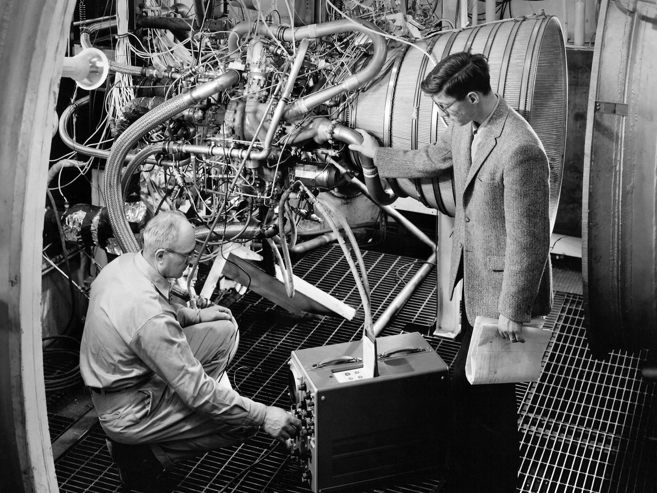 Researchers inspecting a Pratt and Whitney RL-10 rocket engine in a laboratory setting.