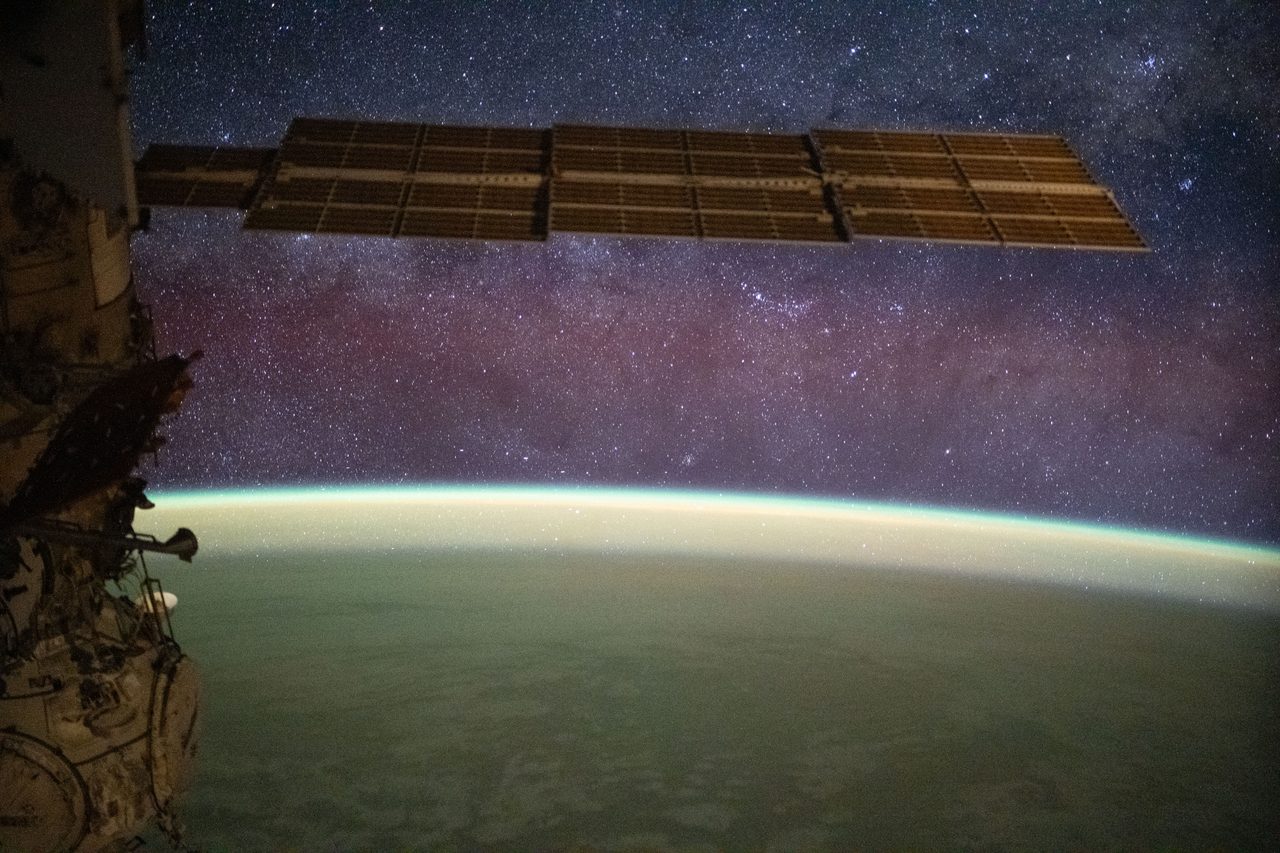 The Milky Way galaxy arches across the night sky, illuminating the landscape with vibrant airglow hues.