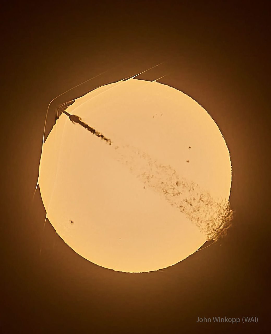 A rocket crossing the sun creates a stunning triple shockwave pattern against a clear blue sky.