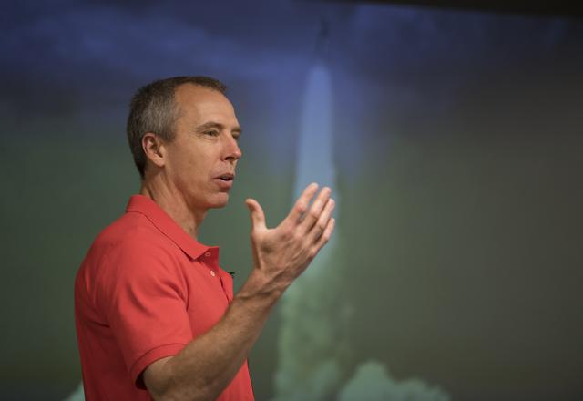 Astronaut Drew Feustel stands at NASA Headquarters, wearing a blue flight suit with mission patches.