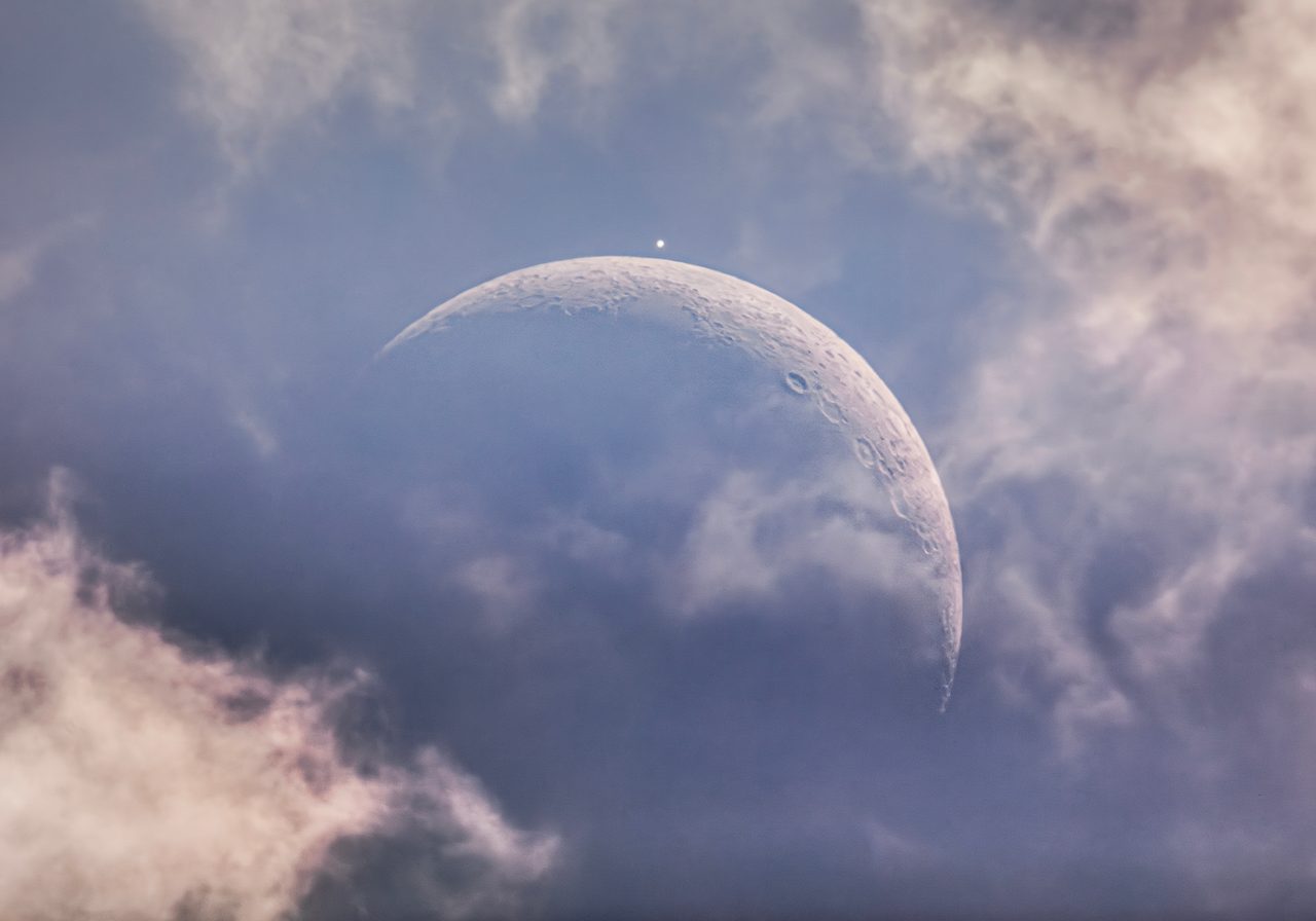 A daytime moon visible in the sky alongside a bright evening star against a clear blue backdrop.