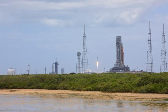 Three rockets, Artemis I, Crew-4, and Starlink, stand ready on launch pads under a clear blue sky.