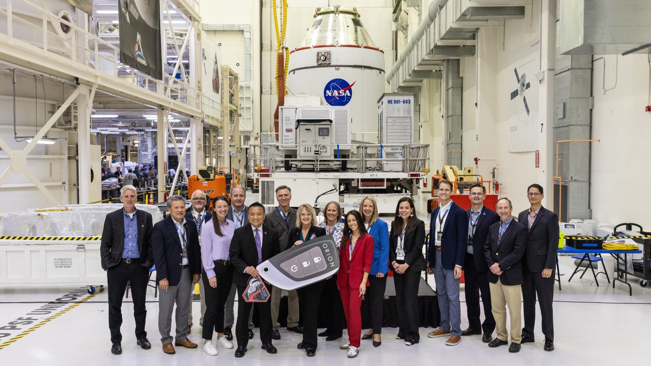 A group of astronauts and officials present Artemis II mission details with a large screen in the background.
