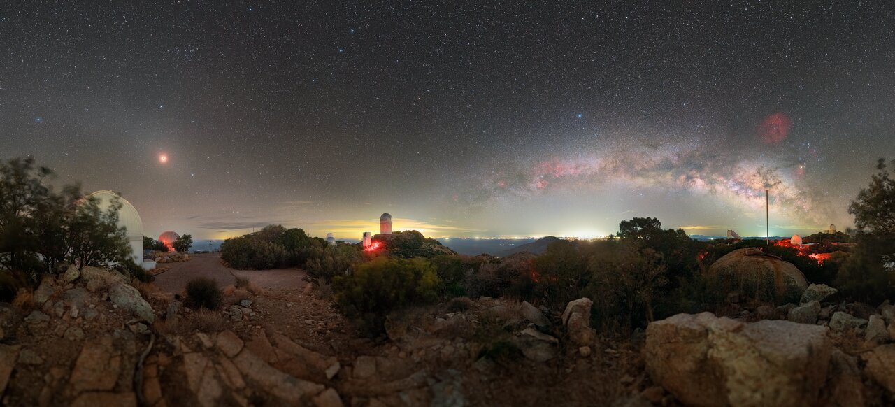 A starry night sky over Kitt Peak Observatory with telescopes silhouetted against the Milky Way.