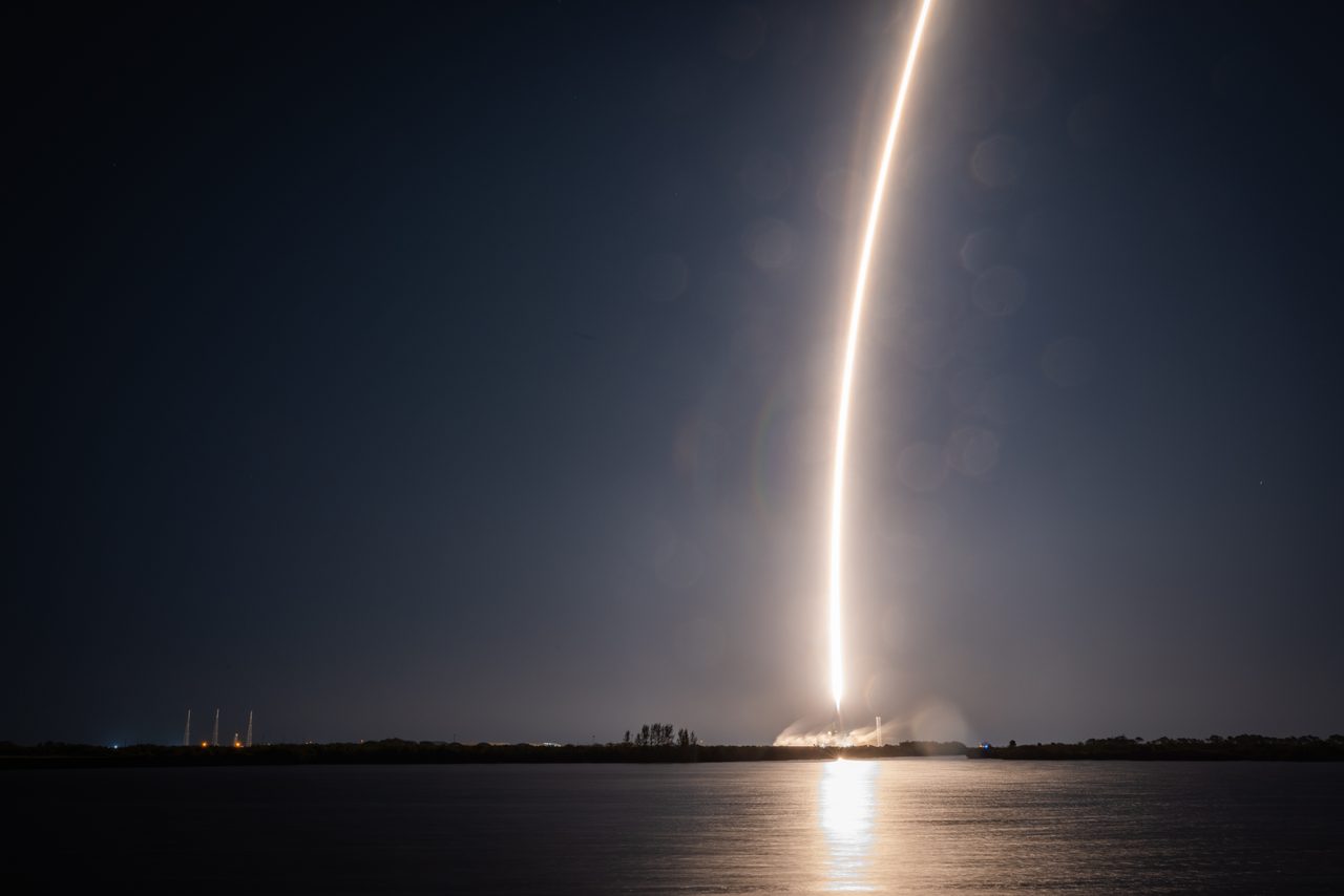 The long-exposure streak of a night rocket launch from Florida, reflected in the water