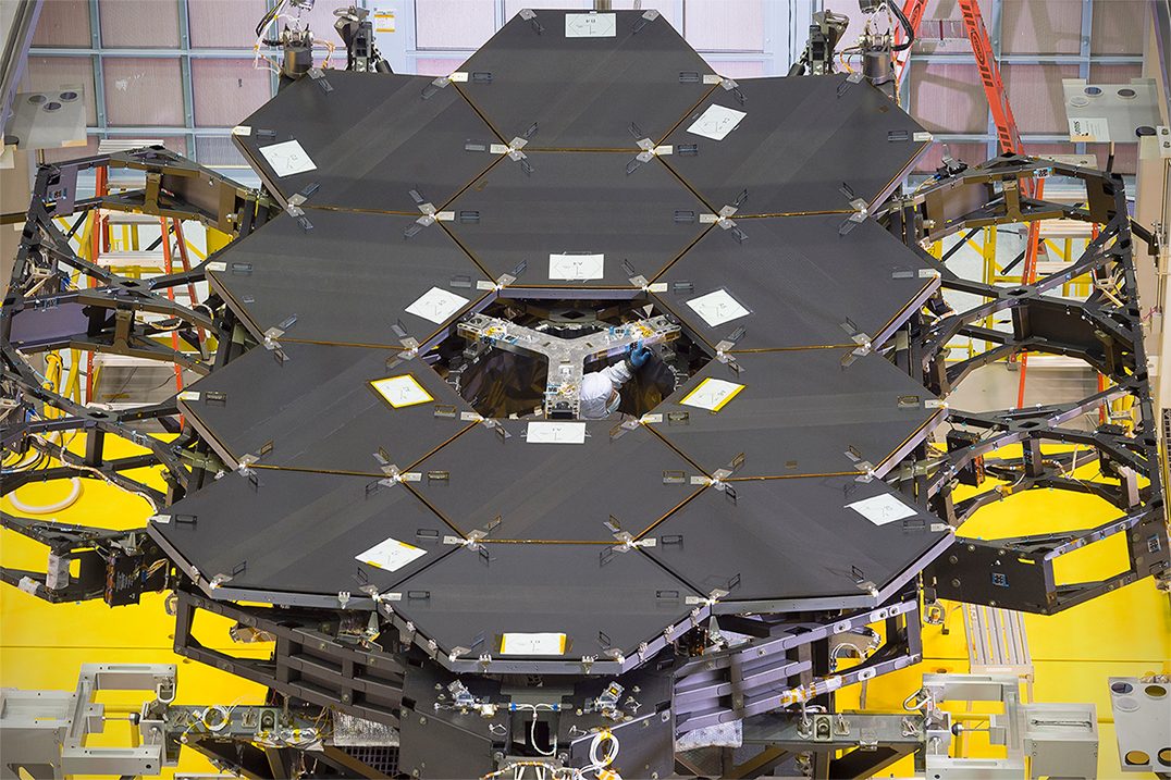 Twelve hexagonal mirrors of the James Webb Space Telescope are displayed, showcasing their reflective gold surfaces.