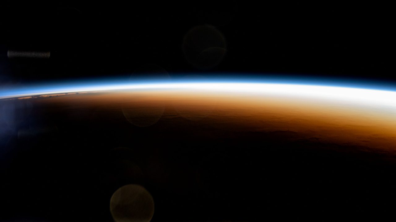 A vibrant orbital sunrise highlights Earth's atmosphere and the terminator line from the International Space Station over the Pacific Ocean.
