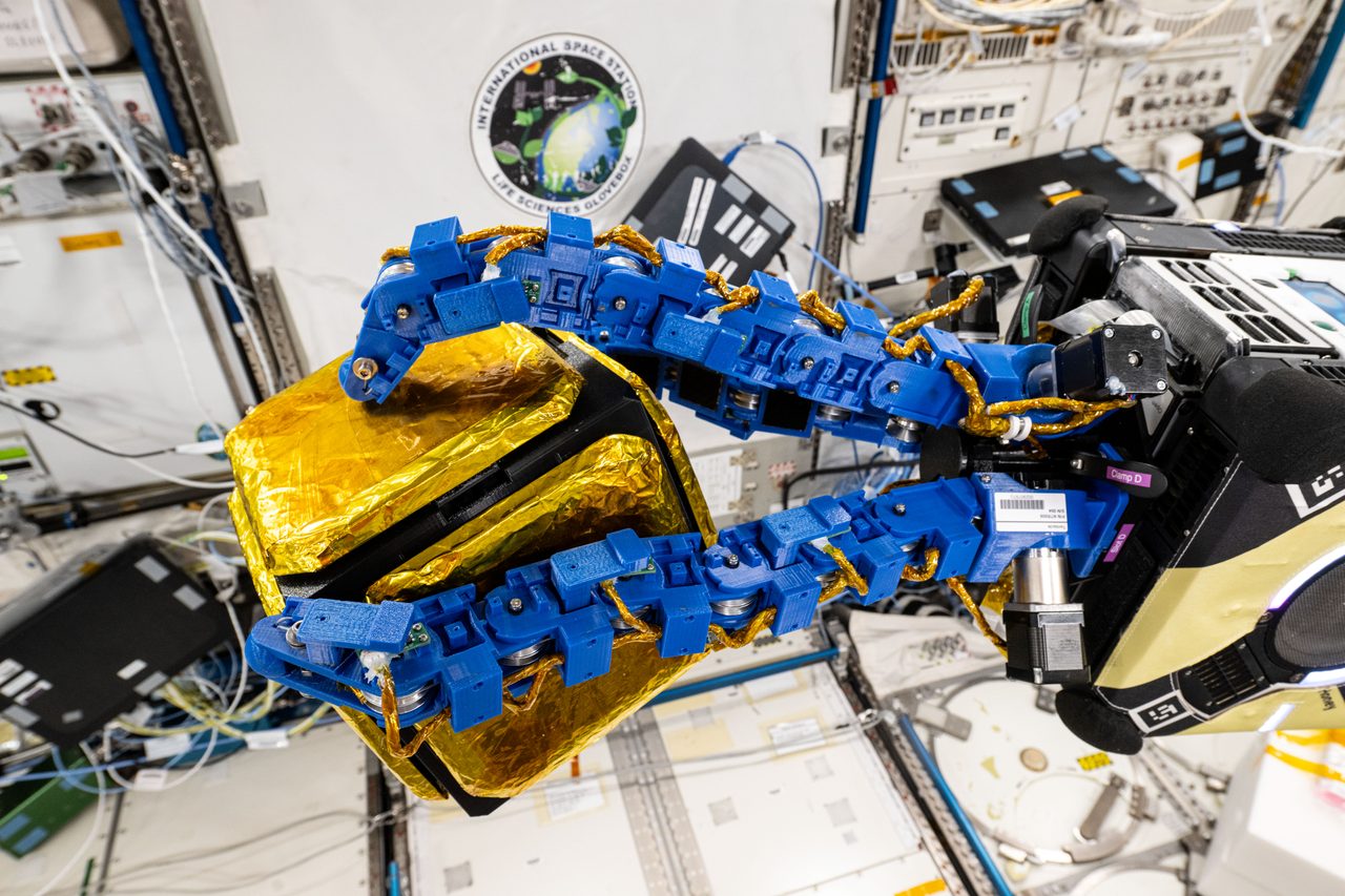 Astrobee robotic free-flyer with flexible blue arms, designed for autonomous operations in space.