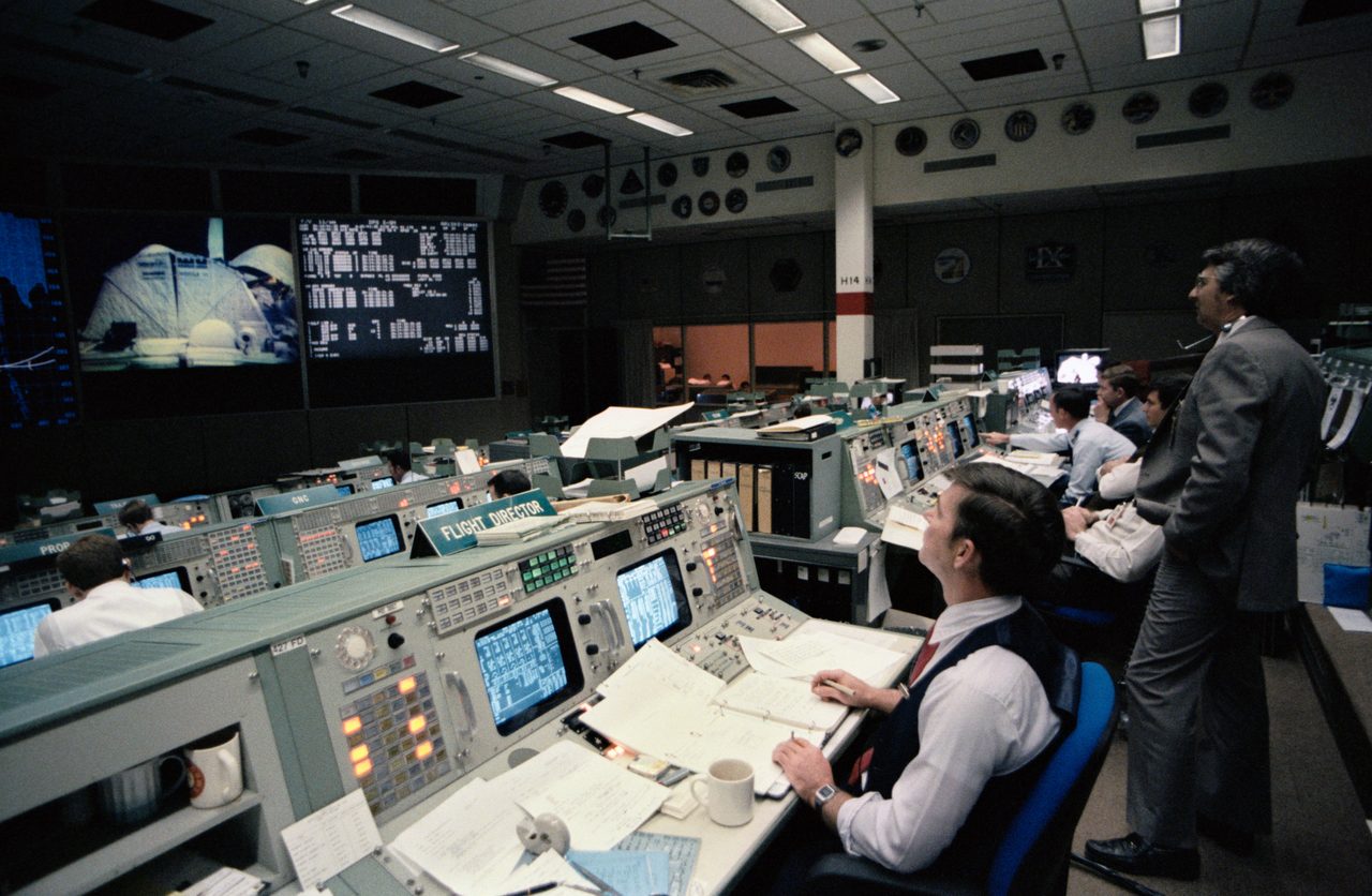 Mission Control Center monitors STS-11/41B space shuttle mission with multiple screens and personnel.