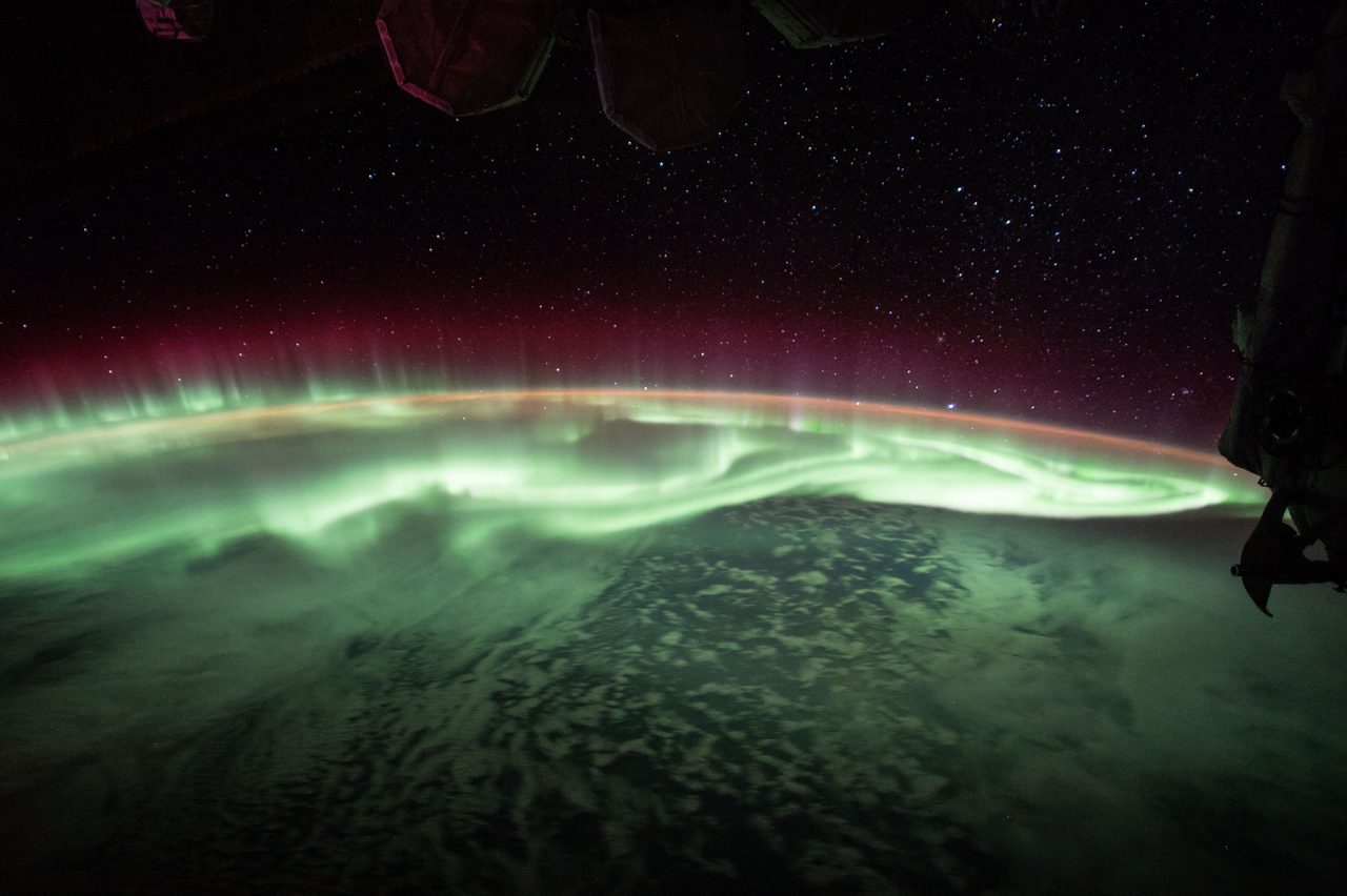 Vivid aurora borealis with green and purple hues illuminating a starry night sky over a serene landscape.