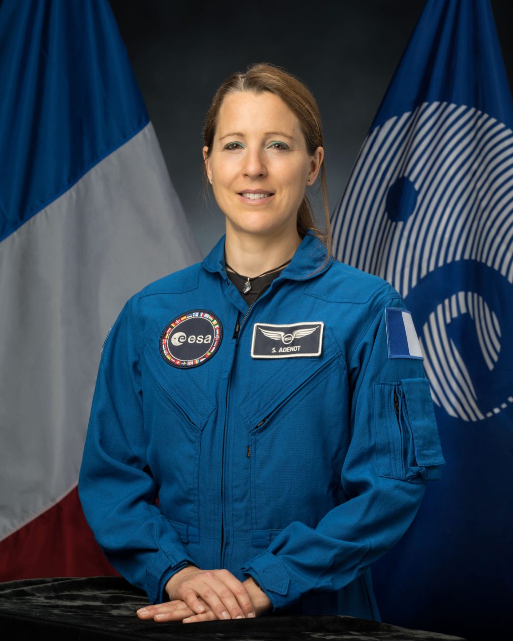 ESA astronaut Sophie Adenot in official portrait at NASA's Johnson Space Center, wearing blue flight suit.