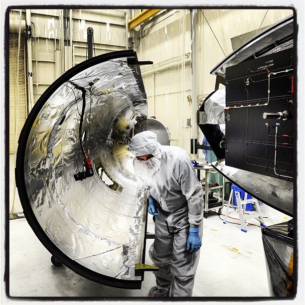 Technicians in clean suits work on NASA's solar satellite inside a sterile room before its upcoming launch.