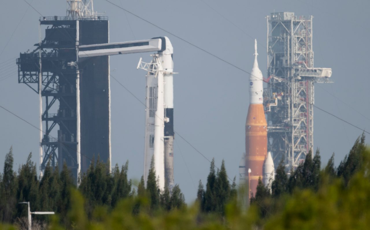 NASA's SLS and SpaceX's Falcon 9 rockets poised at Launch Complex 39A and 39B under clear skies