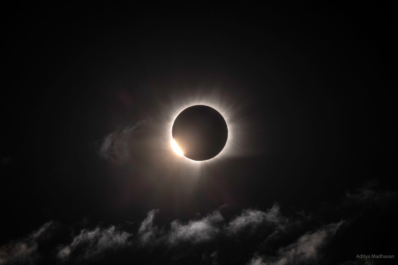 A total solar eclipse casting a shadow over Greenland's icy landscape under a darkened sky.