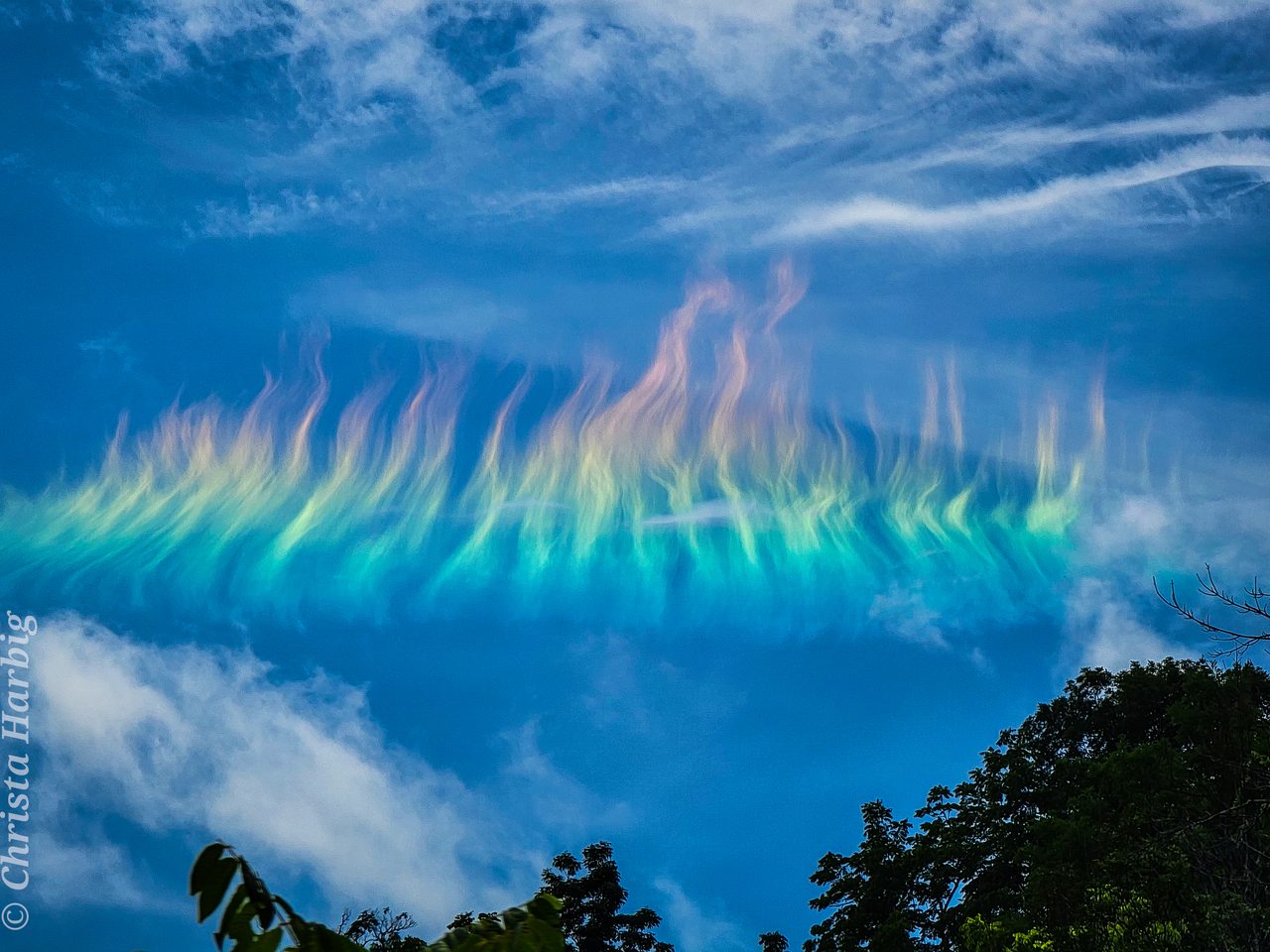 A vibrant fire rainbow arcs across the sky above a lush, green landscape in West Virginia.