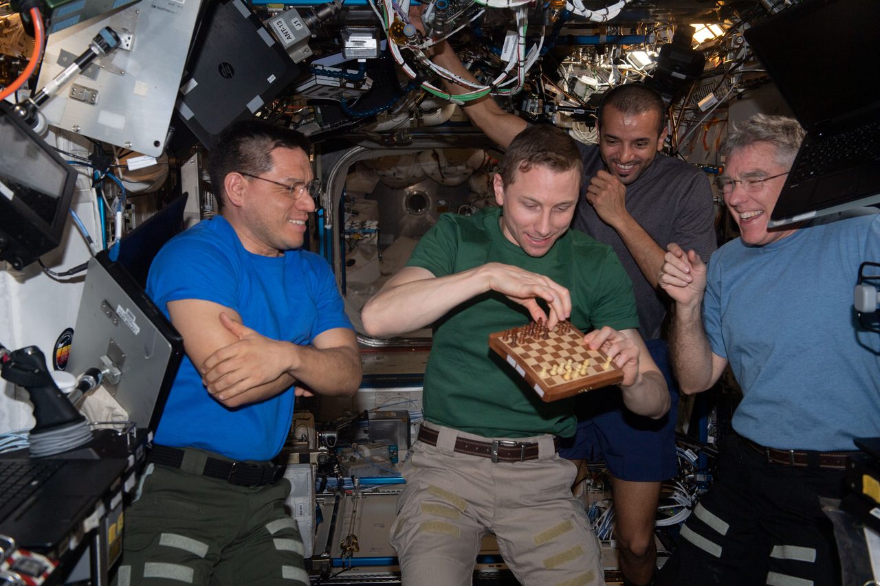 NASA astronaut Woody Hoburg plays chess with mission controllers, surrounded by fellow Expedition 69 crew members.