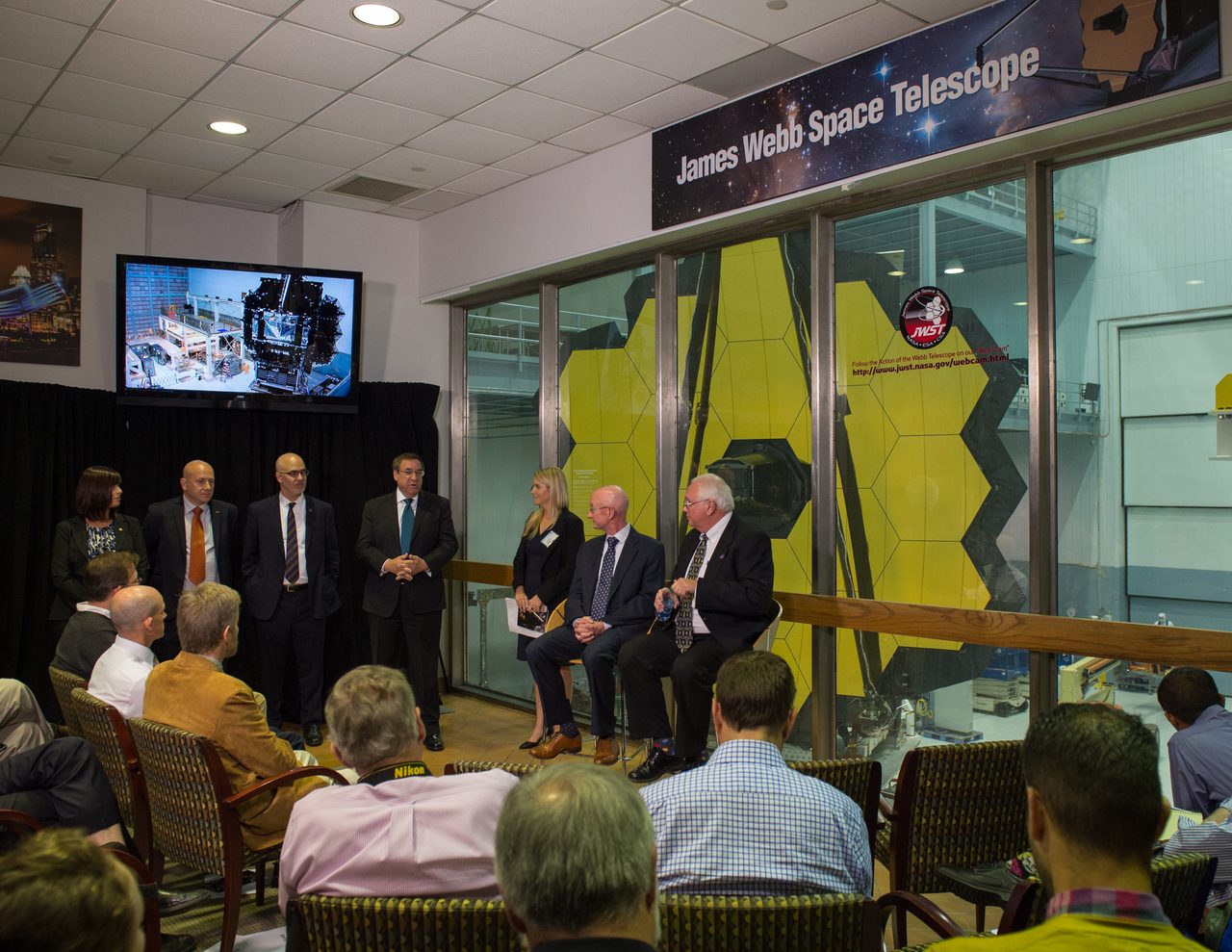 The James Webb Space Telescope's golden hexagonal mirrors are fully revealed, reflecting light in a dark room.