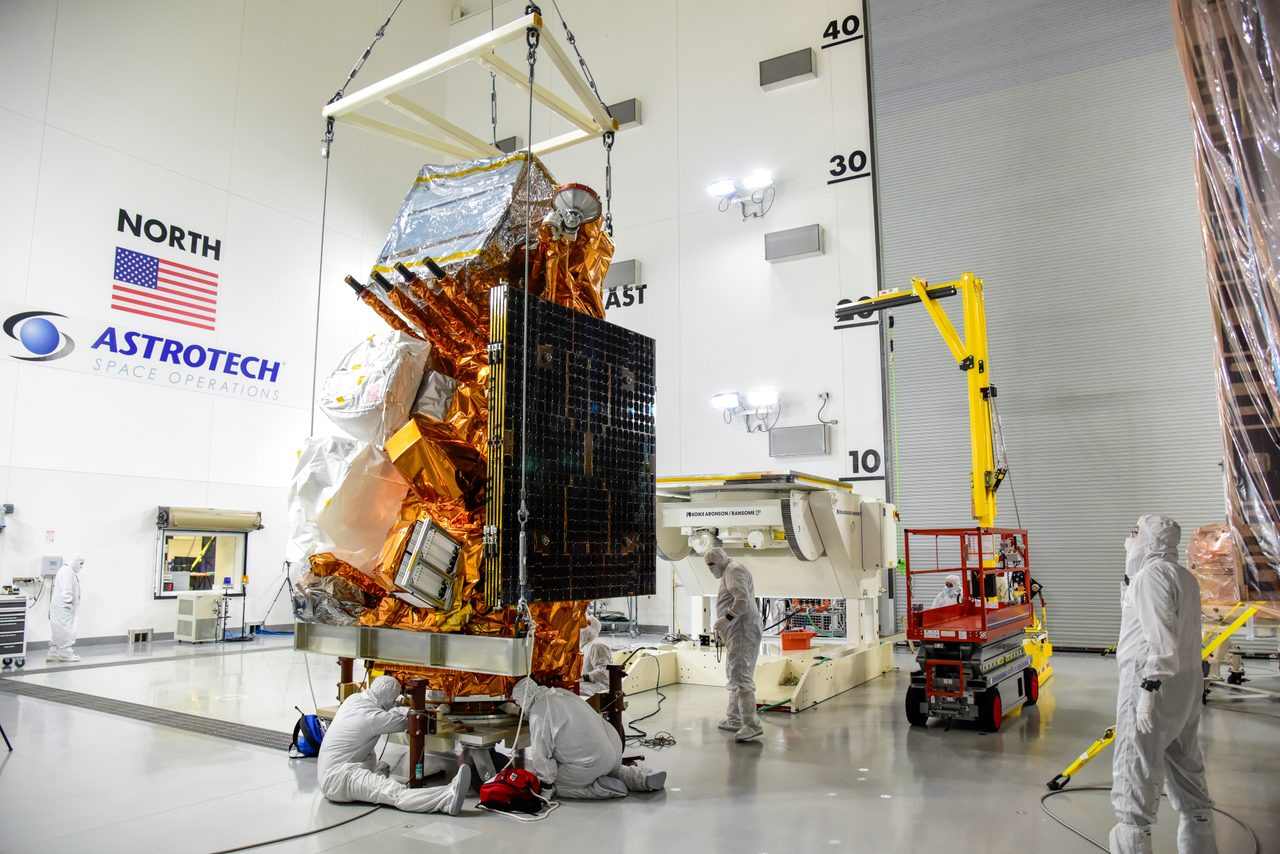Technicians carefully move the JPSS-2 spacecraft onto an integration and testing cart in a cleanroom.