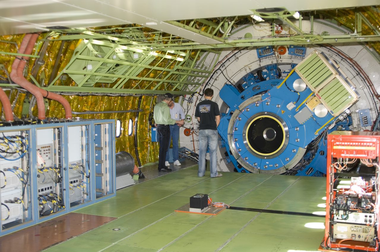 Technicians inspecting the mounting structure of an infrared telescope inside NASA's SOFIA aircraft observatory.