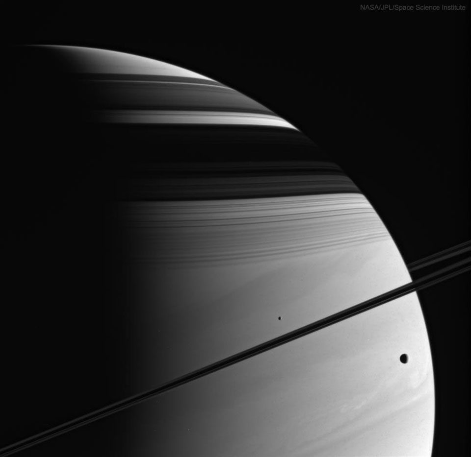A stunning view of Saturn's rings and moons casting shadows on the planet's cloud-covered surface.