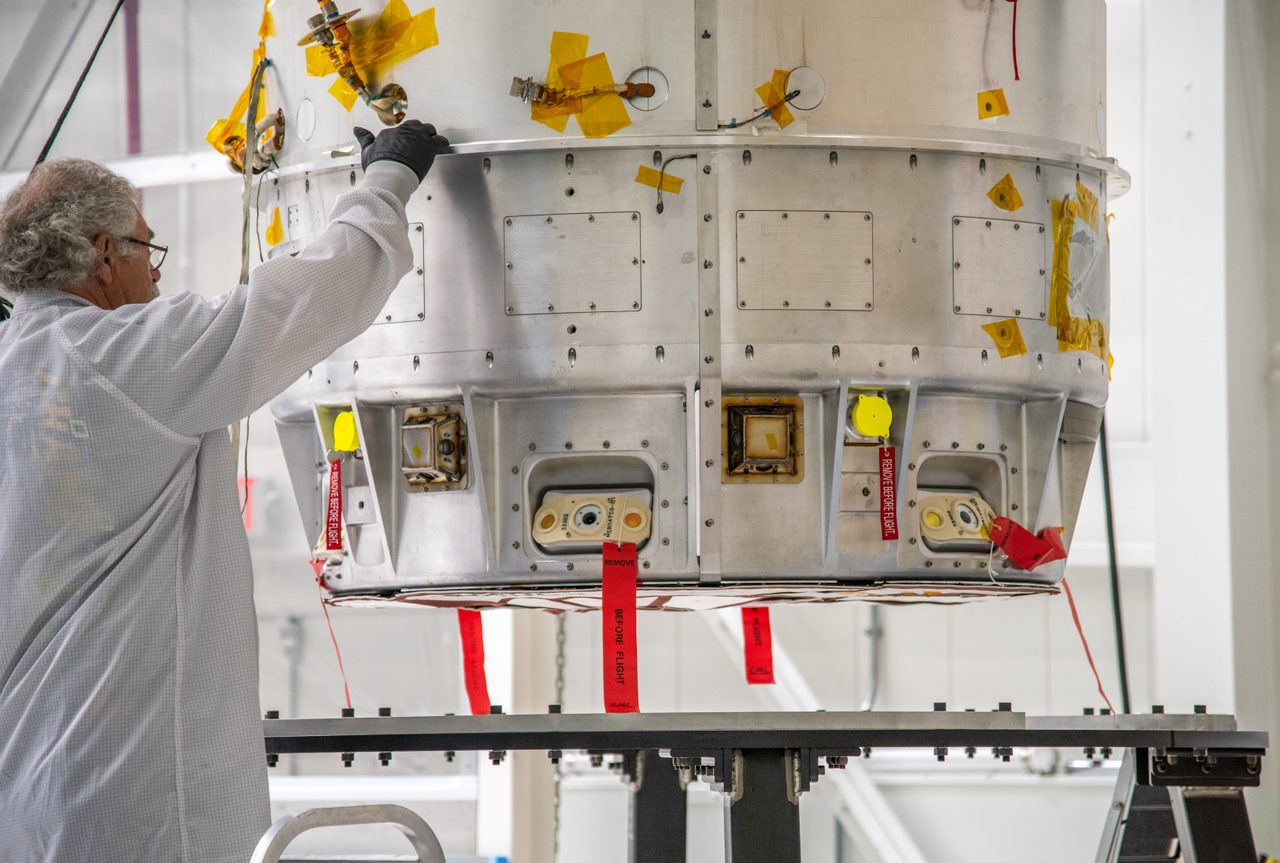 LOFTID spacecraft being carefully lifted by crane onto a work stand inside a spacious facility.