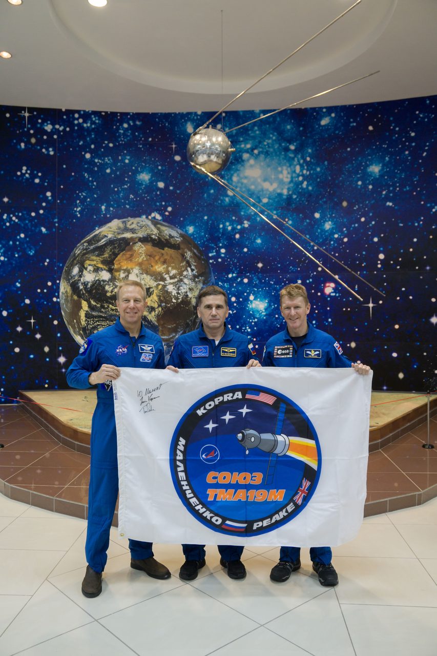 Expedition 46-47 crew members holding mission flag at Korolev Museum, Baikonur Cosmodrome, Kazakhstan.