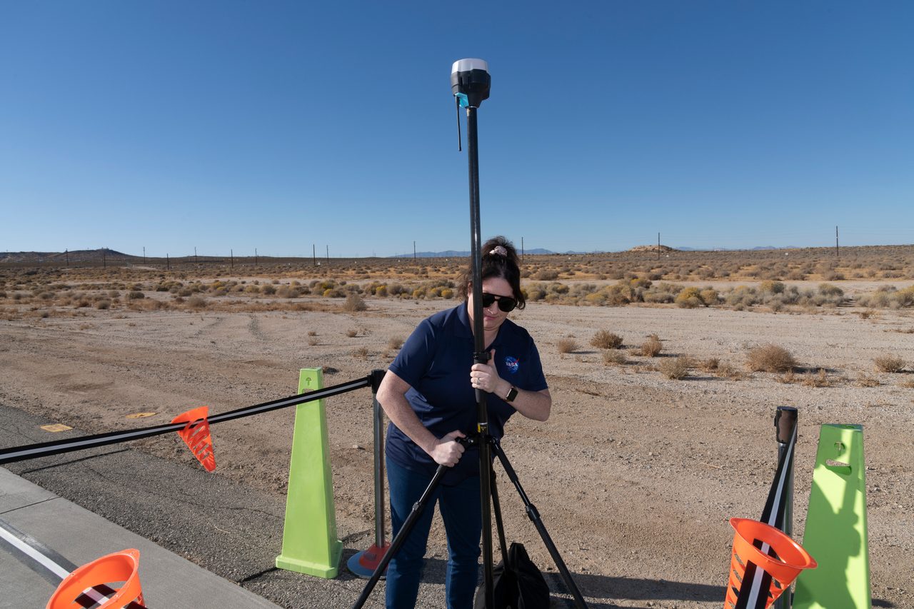 NASA intern Saré Culbertson adjusts tripod-mounted receiver amidst desert landscape at Armstrong Flight Research Center.