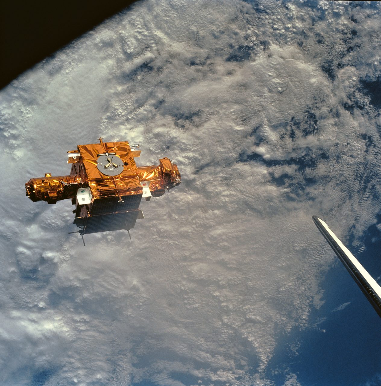 The SPARTAN-201 satellite floating in space with a backdrop of dense cloud formations.