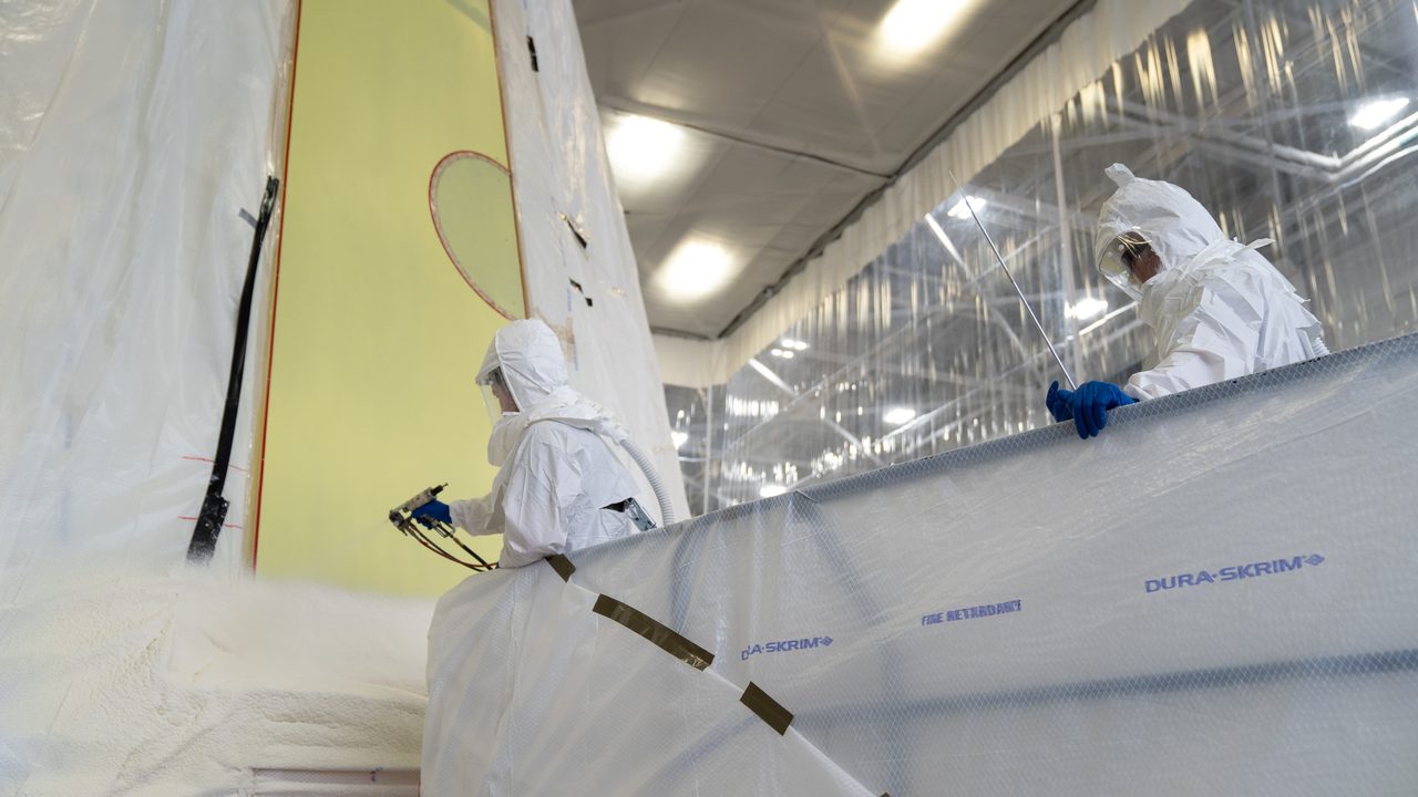 Technicians at NASA's Marshall Space Flight Center apply thermal protection to Artemis III Moon rocket hardware.