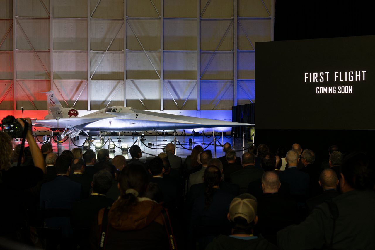 Dimly-lit hangar with NASA's X-59 Quiet Supersonic Aircraft, audience anticipates its first flight.