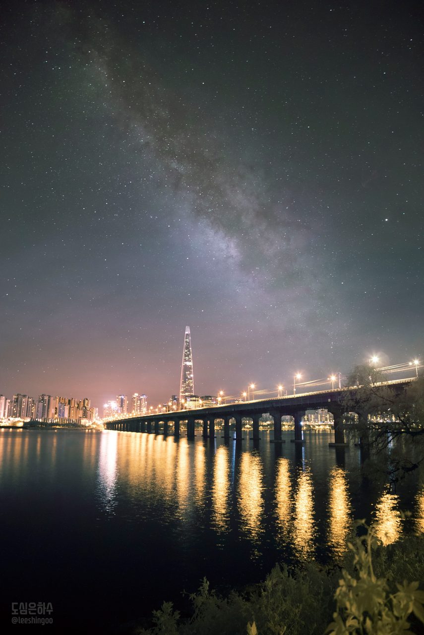 A vibrant night sky with the Milky Way above a city skyline, blending urban and cosmic elements.