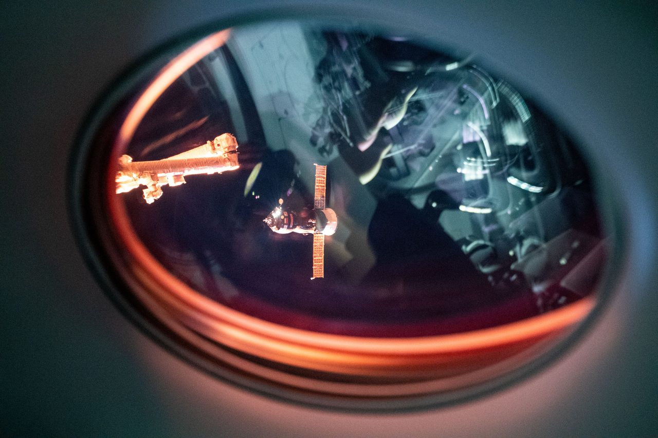 Astronauts working outside the International Space Station during a spacewalk, with Earth visible in the background.