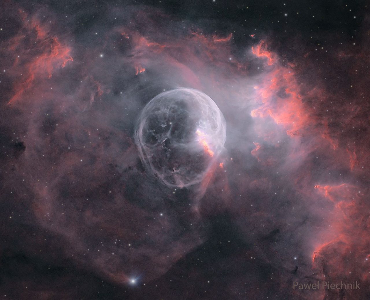 A vibrant cosmic scene showing the Bubble Nebula, a spherical cloud of gas and dust in deep space.
