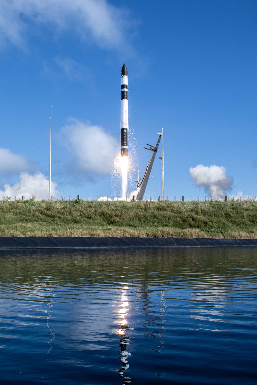 A rocket launches into the sky, leaving a trail of smoke against a clear blue backdrop.