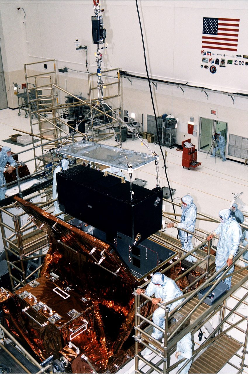 Technicians lower NICMOS instrument into carrier at Kennedy Space Center for Hubble servicing mission.