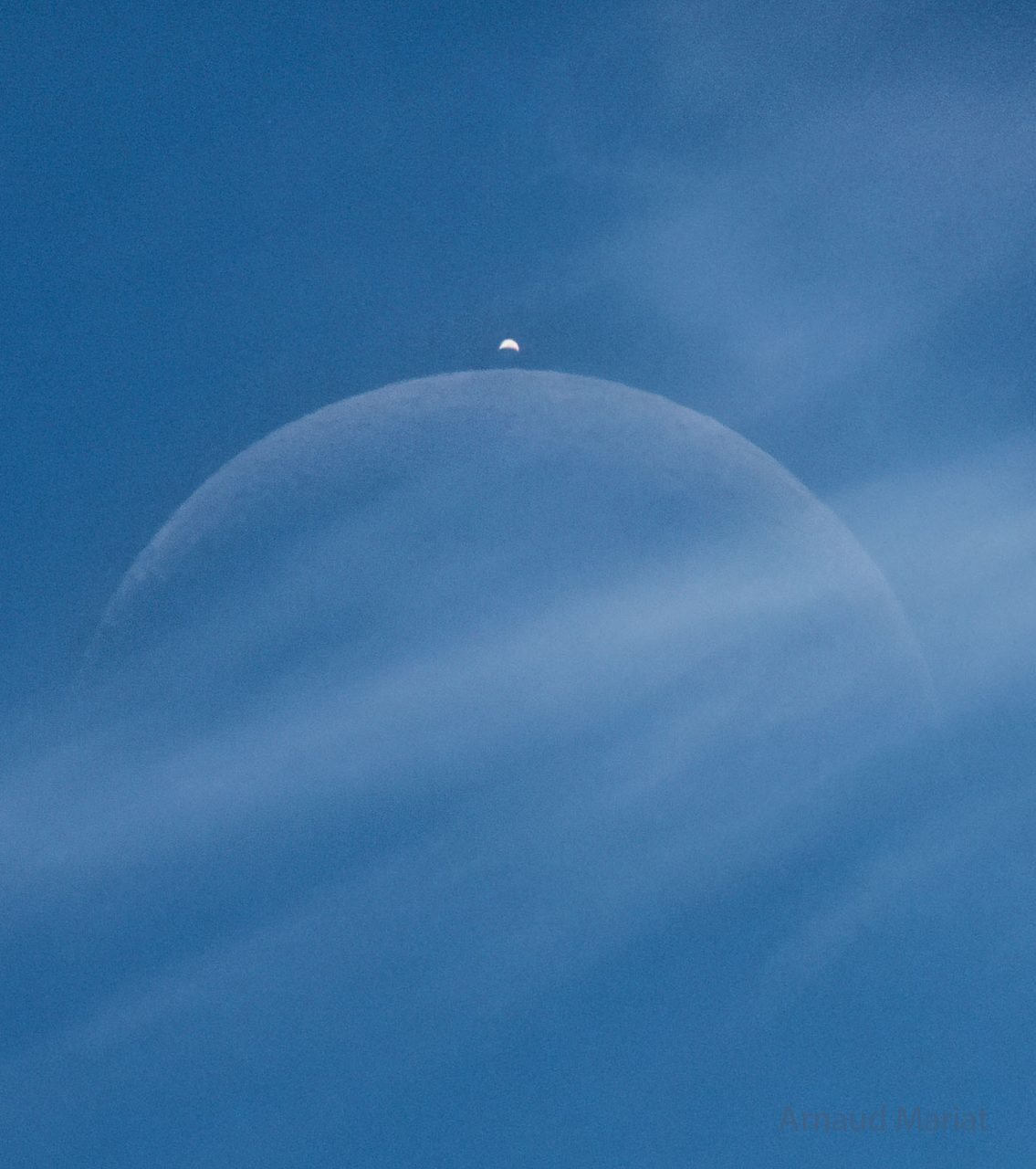 A rare daytime eclipse where the moon partially covers Venus against a bright blue sky with scattered clouds.