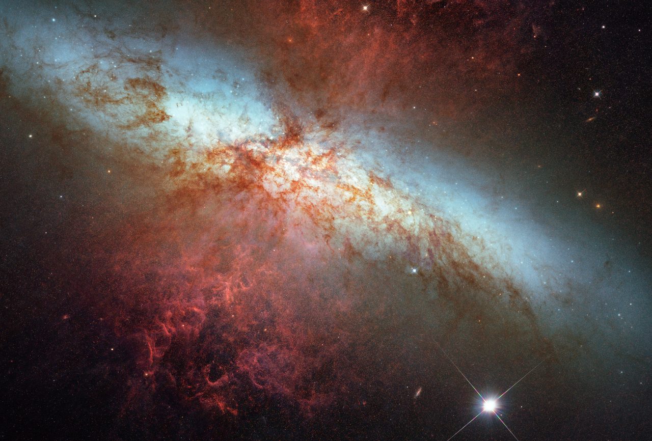 Hubble Space Telescope captures a supernova explosion in galaxy M82, showcasing vibrant cosmic colors.