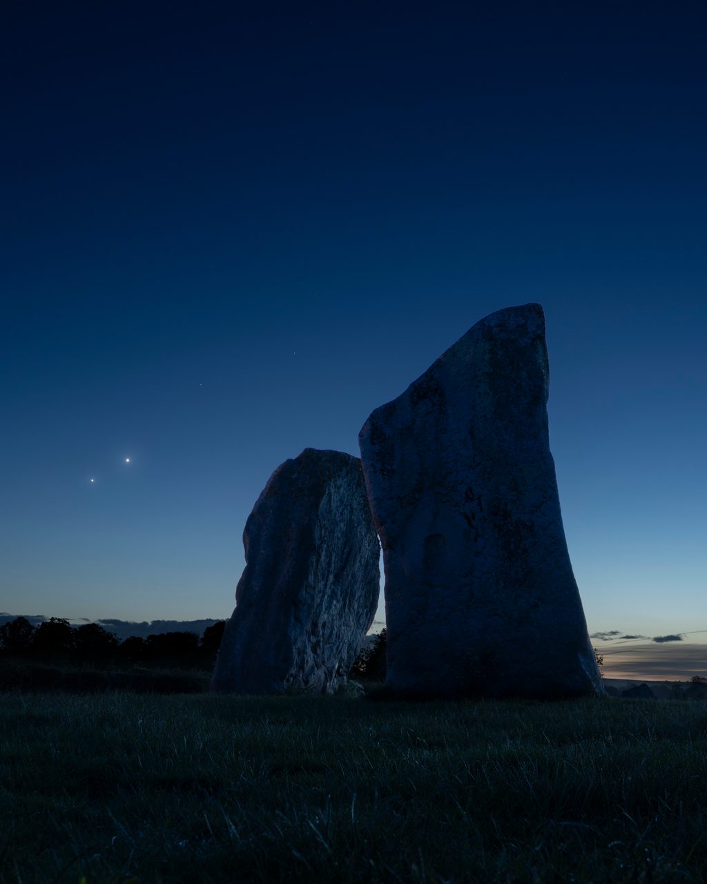 Bright Venus and Jupiter conjunction over ancient stone circle at Avebury during twilight sky.