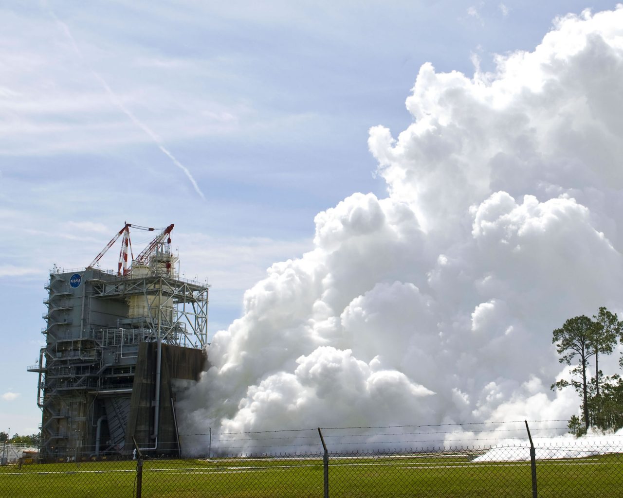 A powerful space shuttle engine test with flames and smoke billowing from the launch pad.