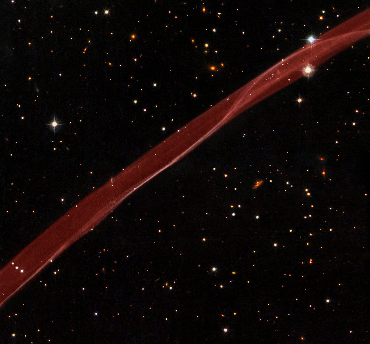 Hubble captures a vibrant celestial scene with stars and a prominent stripe of colorful interstellar gas