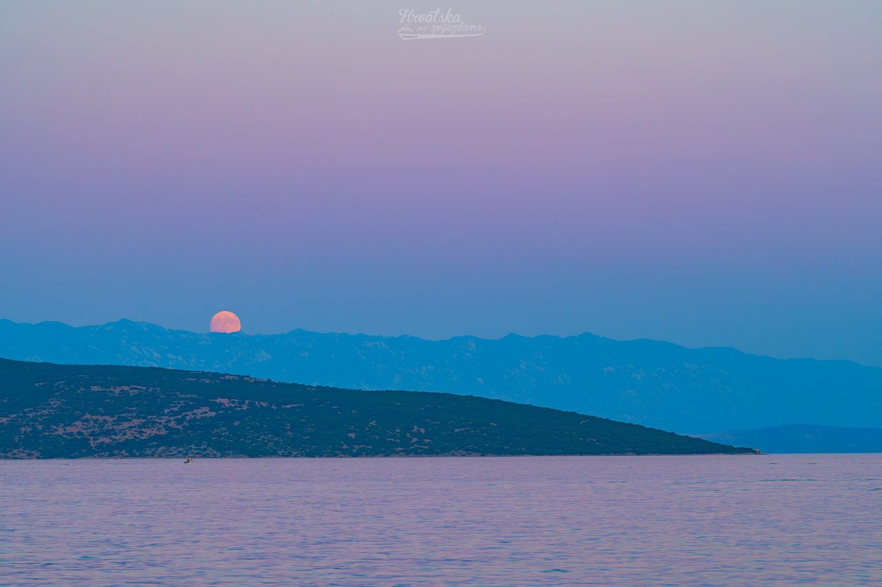 A large Buck Moon rises against a pink and blue Belt of Venus sky at dusk.